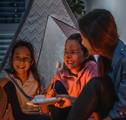 Eine Familie sitzt im dunklen Kinderzimmer in einem Kinderzelt, die Rollos sind heruntergefahren.